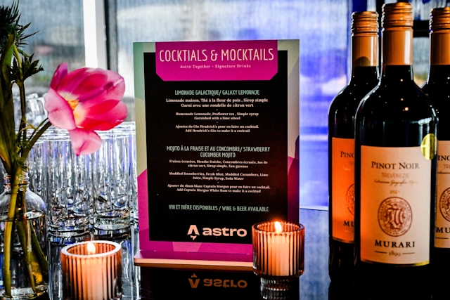 Cocktail and mocktail menu atop a black bar adorned with florals, candles, and wine bottes.