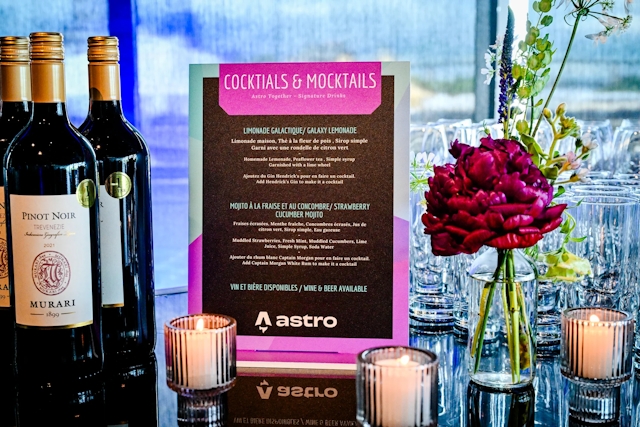 Cocktail and mocktail menu atop a black bar adorned with florals, candles, and wine bottles.