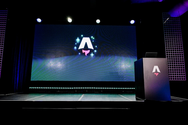 An empty stage with a large LED screen displaying the Astro Together logo. To the right, a black podium branded with the Astro logo.