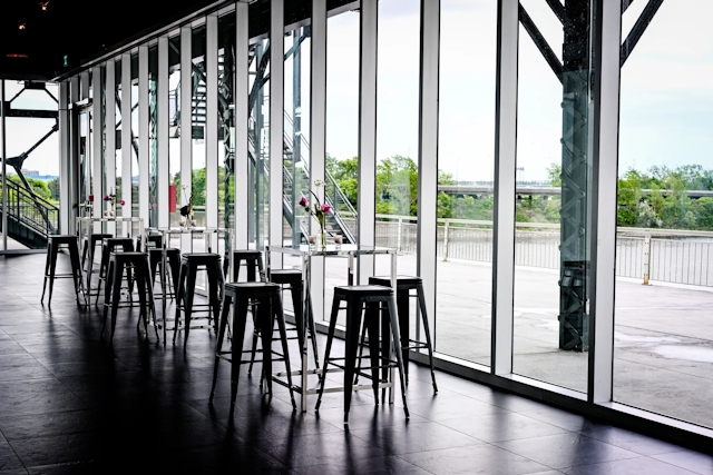 Several high tables and high chairs in front of floor-to-ceiling windows.