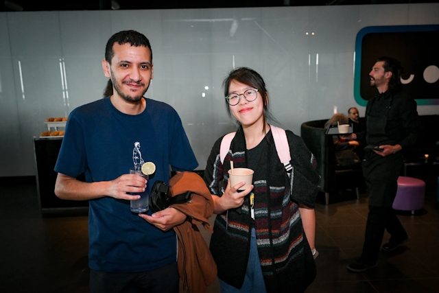 A man holding a purple cocktail poses with a woman holding an appetizer. 