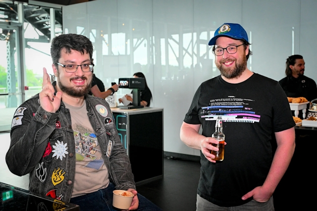 Two glasses-wearing male guests smile and pose together with their food and drink.