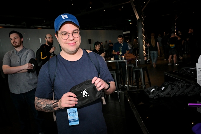 A man holding up a black belt bag branded with the Astro Together logo in white.