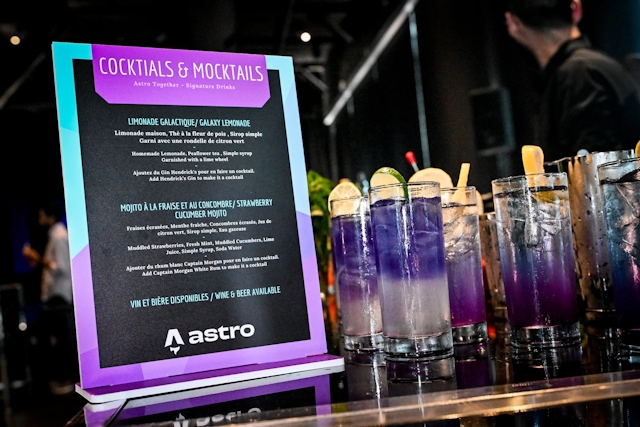 Closeup of cocktail and mocktail menu with purple cocktails in tall glasses off to the right.