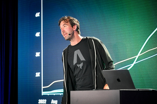 Fred K. Schott on stage in front of a slide depicting a graph, standing next a podium with a laptop sitting atop it.