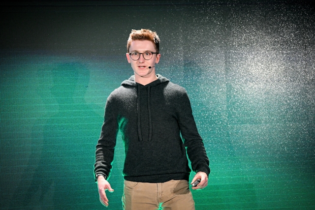 Ben Holmes on stage in front of a green and black LED screen.