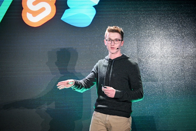 A close up of Ben Holmes on stage in front of a slide depicting logos of other frameworks.