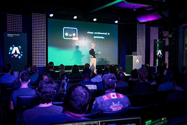 View from the back of the audience. Ben Holmes is on stage in front of a slide with Houston on it as well as a code snippet for an Image component.