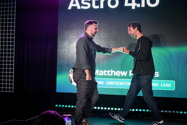 Fred K. Schott fist-bumps Matthew Phillips as he heads off stage and Matthew heads on stage to speak next.