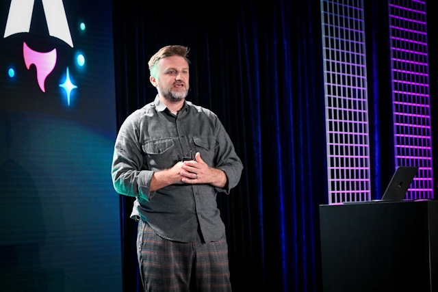 Matthew Phillips speaking on stage next to a podium with a laptop on it. Behind him is the Astro Together logo on-screen.