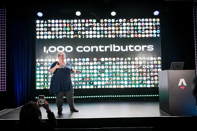 Sarah Rainsberger speaking from the left side of the stage, talking about how Docs has had 1,000 contributors to-date.