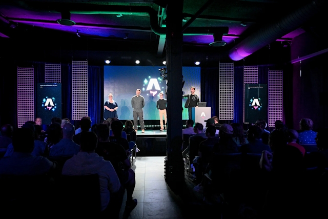 View from the back of the audience. Keynote speakers on stage. From left to right: Sarah Rainsberger, Matthew Phillips, Ben Holmes, and Fred K. Schott (next to the podium).