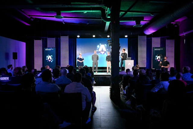 View from the back of the audience. Keynote speakers on stage. From left to right: Sarah Rainsberger, Matthew Phillips, Ben Holmes, and Fred K. Schott (next to the podium).