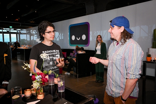 Two guests chat at a high table with their drinks. In the background, the Houston lounge can be seen.