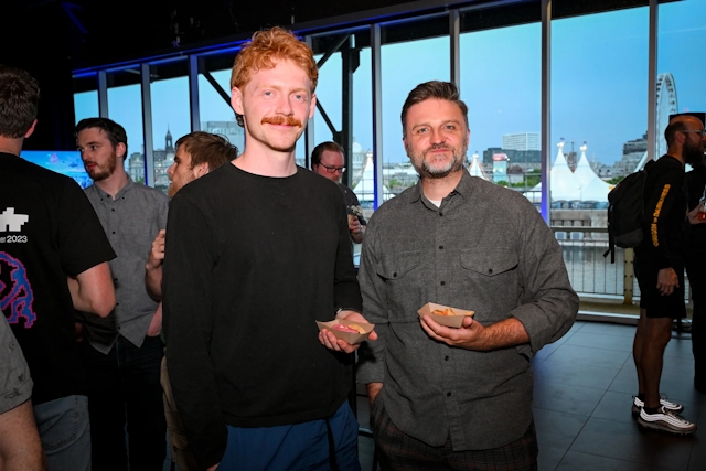 Matthew Phillips poses with a guest while they hold tacos.