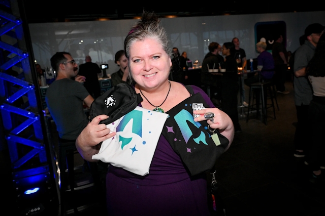 A guest holds up her white and black Astro logo printed t-shirts along with a black belted bag branded with the Astro logo in white.